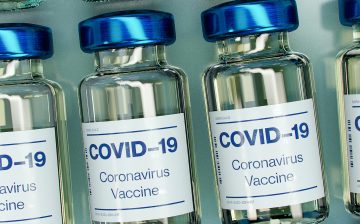 A photo of four vials of COVID-19 vaccine with blue lids