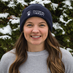 Robin is smiling outside wearing a physical therapy toque. There is snow on a tree behind her.