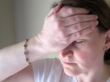 A women with a mild traumatic brain injury, more commonly known as a concussion, holds her hand against her head.