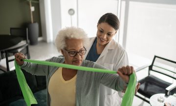 A physician helps an elderly patient perform exercises with a resistance band.