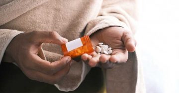 A man's hand with pills spilled out of the container.