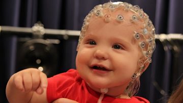 A smiling infant wearing an electroencephalography (EEG) listens to a rhythmic pattern.