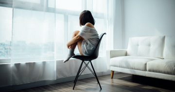 A woman sitting on black chair in front of glass-panel window with white curtains.