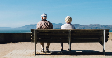 A man and woman sitting on a bench facing the sea.