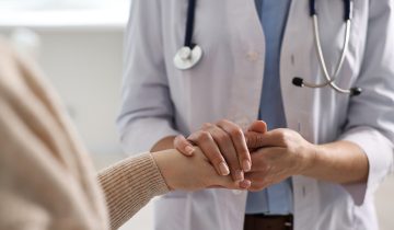 A doctor in white attire with a stethoscope comforts a patient.