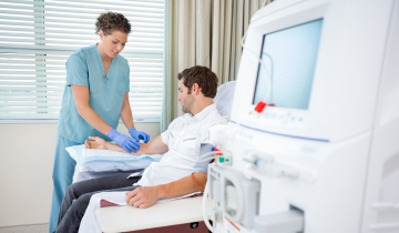 A healthcare worker preparing a patient's arm for dialysis, with a dialysis machine in view.