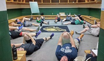 A group of participants lies in a circle engaging in a floor exercise during a Hockey FIT training session.