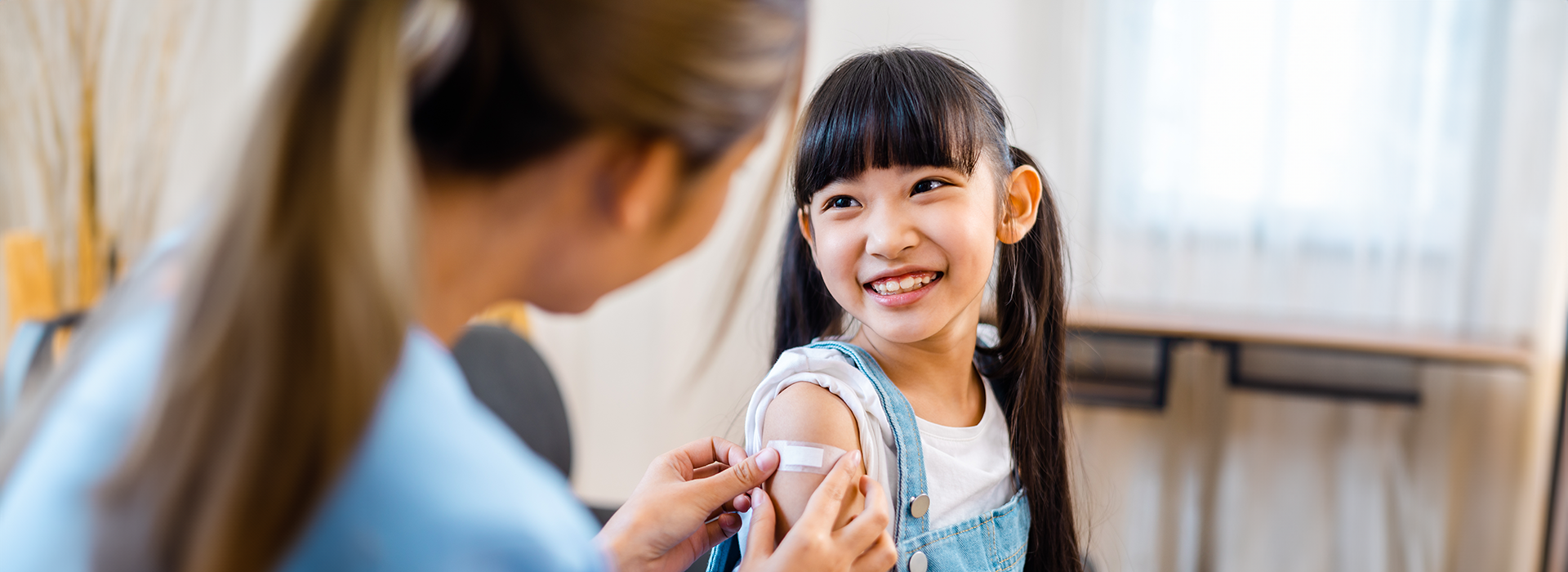 A healthcare worker puts a bandage on a smiling girl's arm after a vaccination.