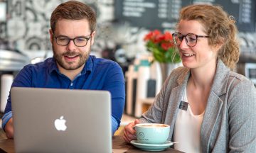 Drs. Brian Hayes and Hannah Young sit at a table, smiling and engaged while working on a laptop.